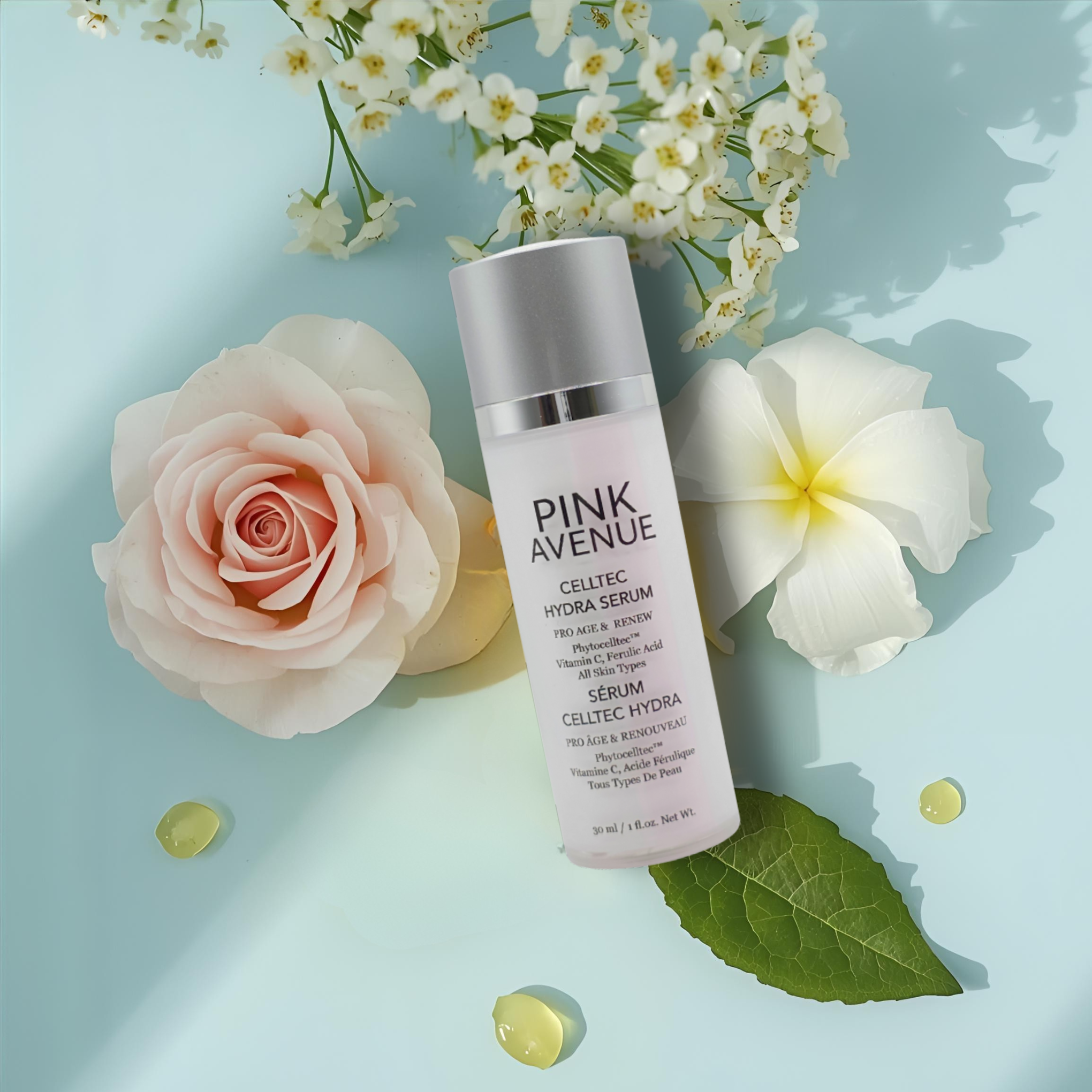 Pink Avenue serum bottle surrounded by flowers, alpine rose, gardenia, argan oil drops on a light blue background
