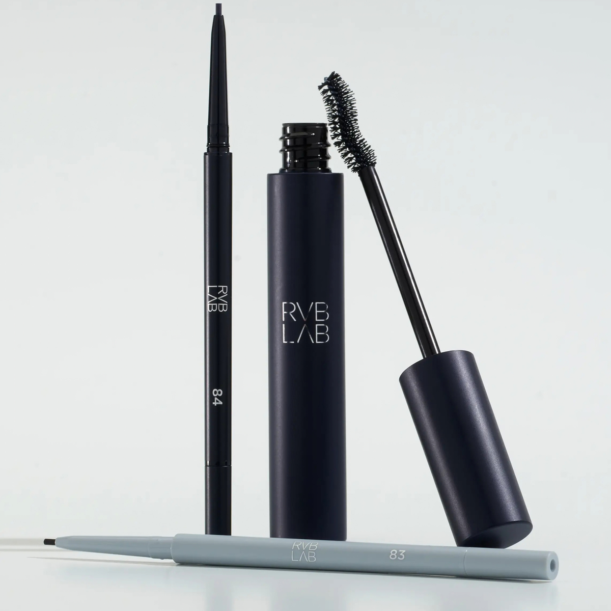 Two black cosmetics pencil and mascara from RVB LAB,Makeup one standing vertically and one lying horizontally, shown with their applicator wand on a clean white background.