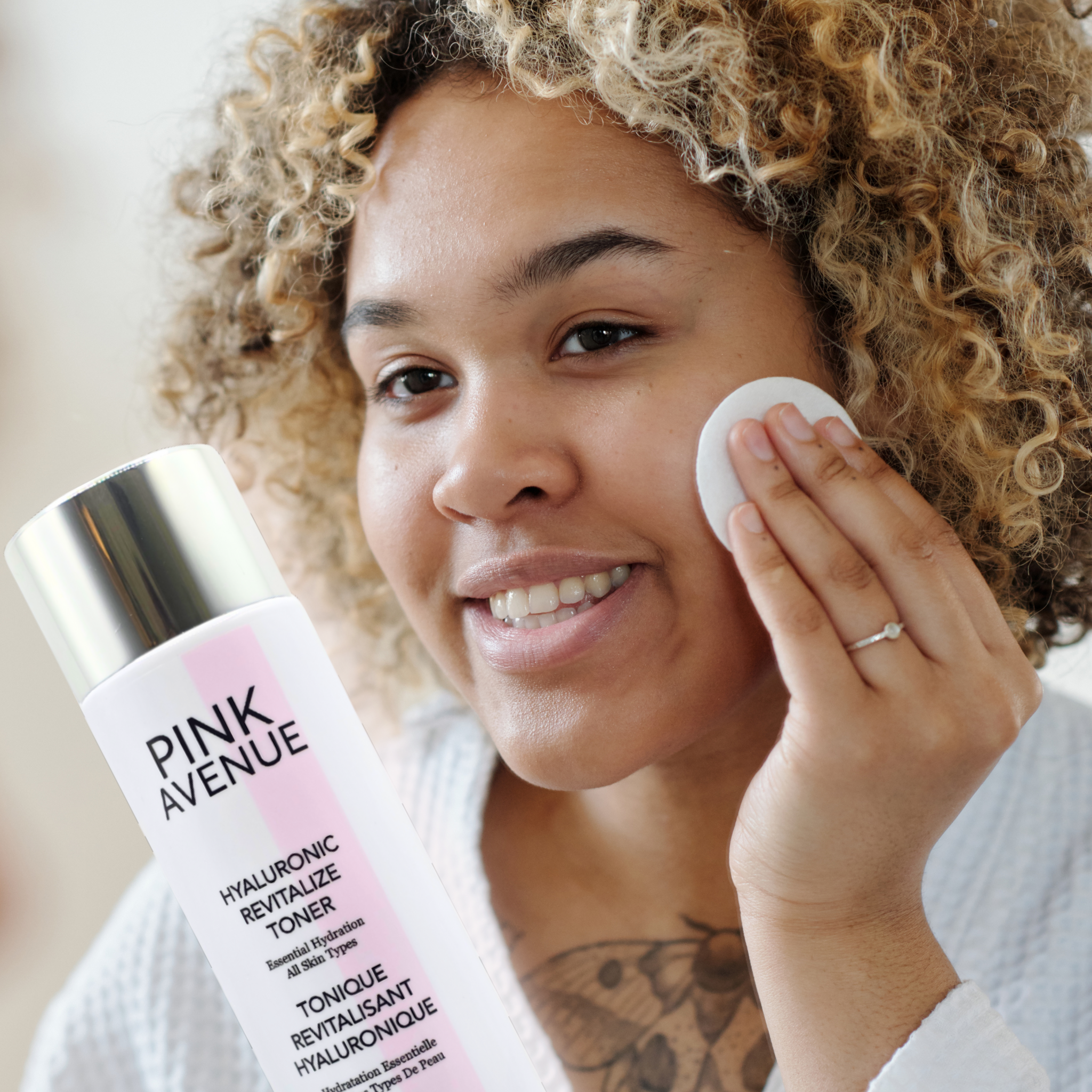 Woman applying toner with a cotton pad, holding a 'Pink Avenue' toner bottle.
