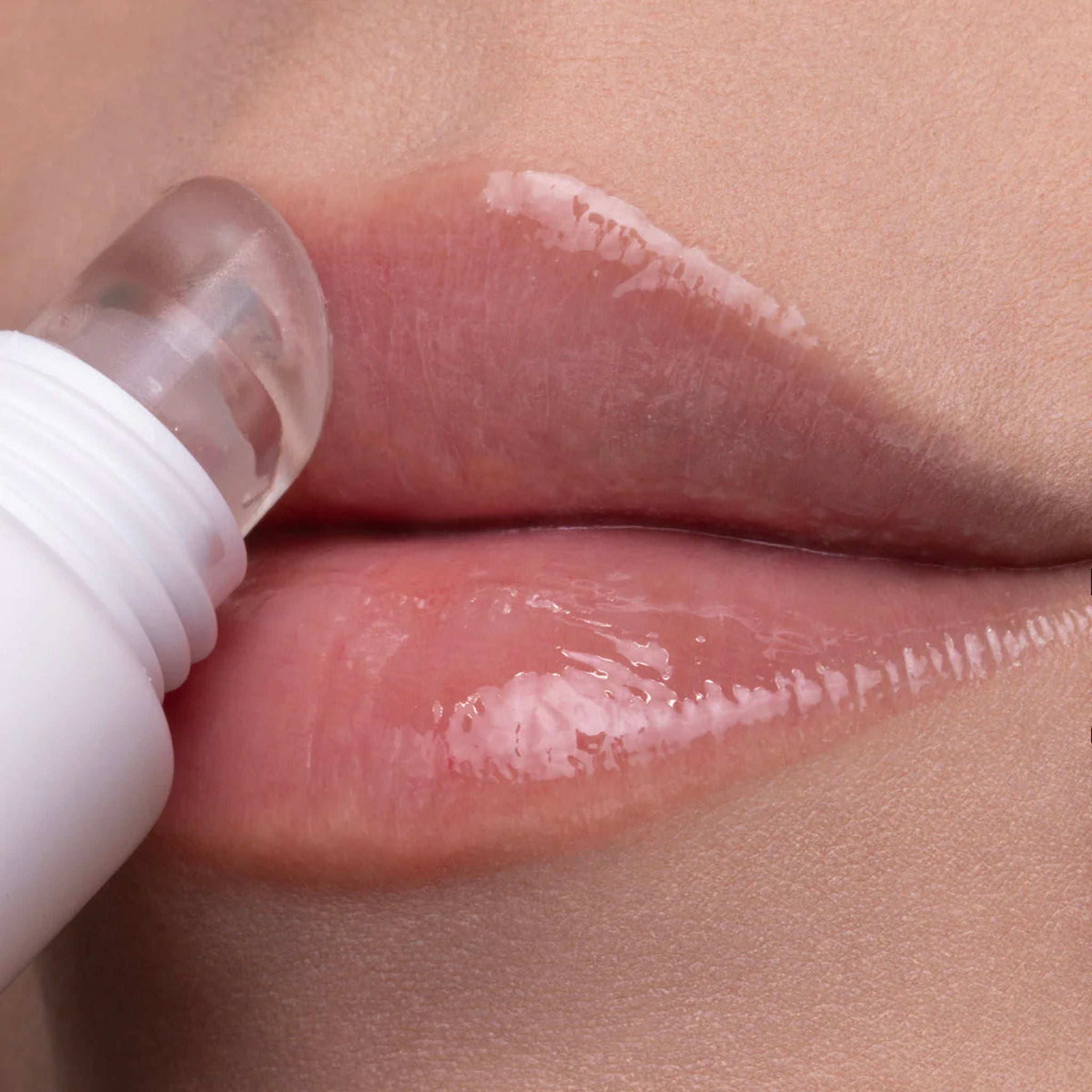 Close-up of a person's lips applying a glossy lip product from a white tube with a clear rounded applicator tip.