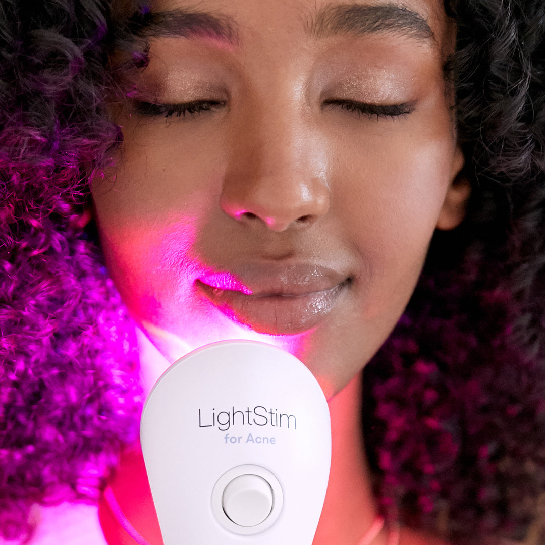 Woman using LightStim for Acne LED light therapy device with pink and blue lights illuminating her face